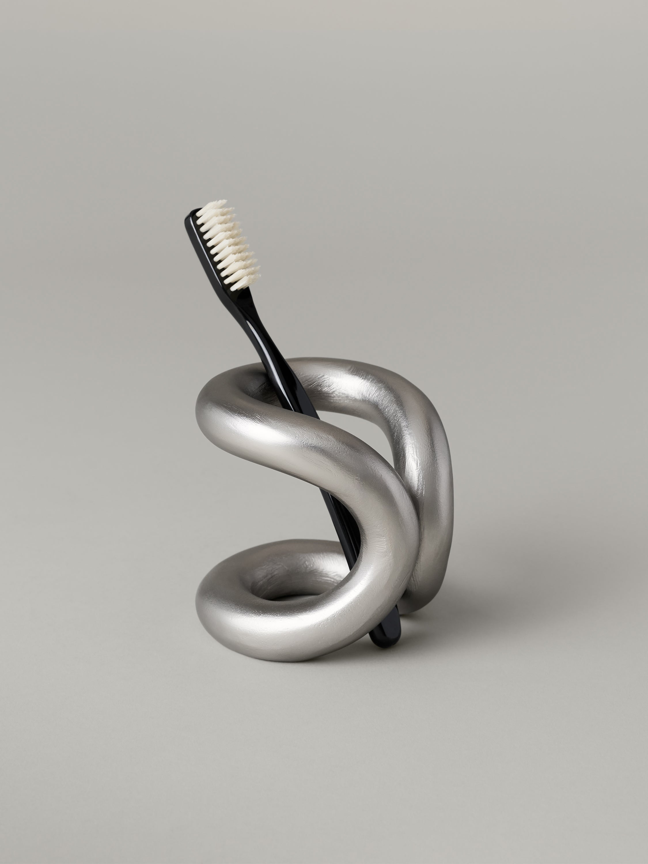 Aluminum toothbrush holder with a cantilevered form and open coil base
