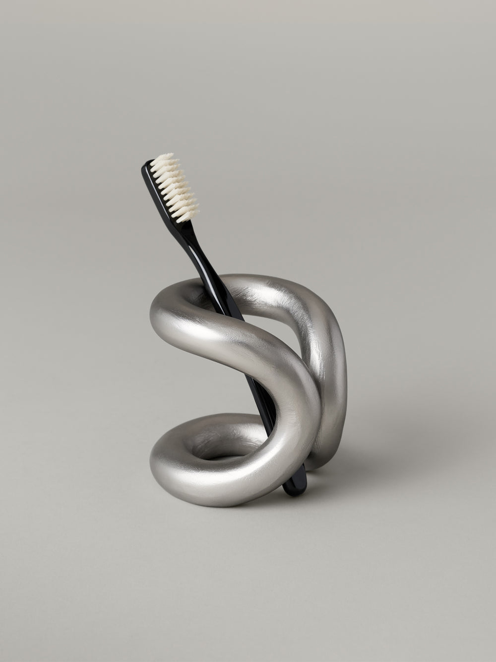 Aluminum toothbrush holder with a cantilevered form and open coil base